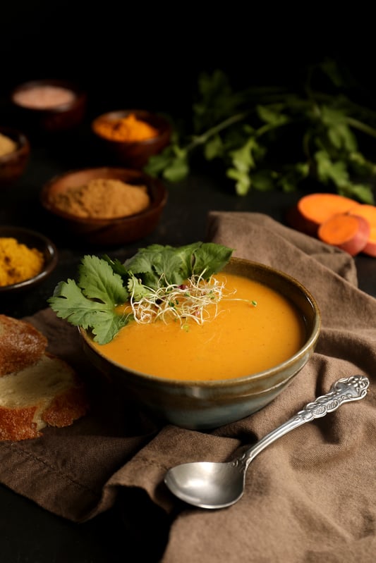 Sweet potato soup with coconut curry is delicious and warming with Indian spices like cinnamon and curry powder. Soup is garnished with fresh cilantro, sprouts, and crispy bread. 