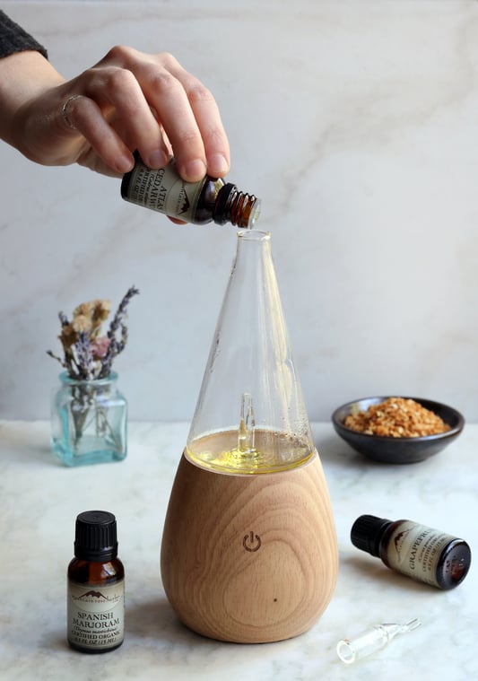Hand pouring drops of essential oil into diffuser to make spanish marjoram aroma diffuser blend