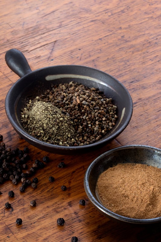 Hulled cardamom, black pepper and peppercorns, cinnamon powder and other spices in bowls on wooden table
