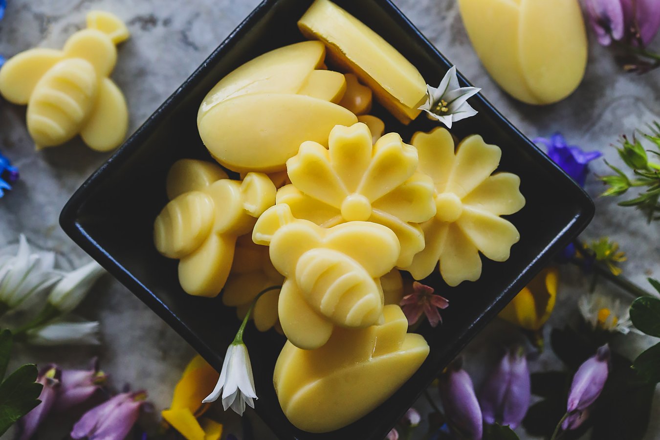 Spring Wax Melts in the shapes of bees and flowers sitting in a bowl- surrounded by fresh flowers. 