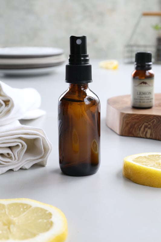 Amber glass mister bottle with lemon spray and lemon essential oil on counter for cleaning