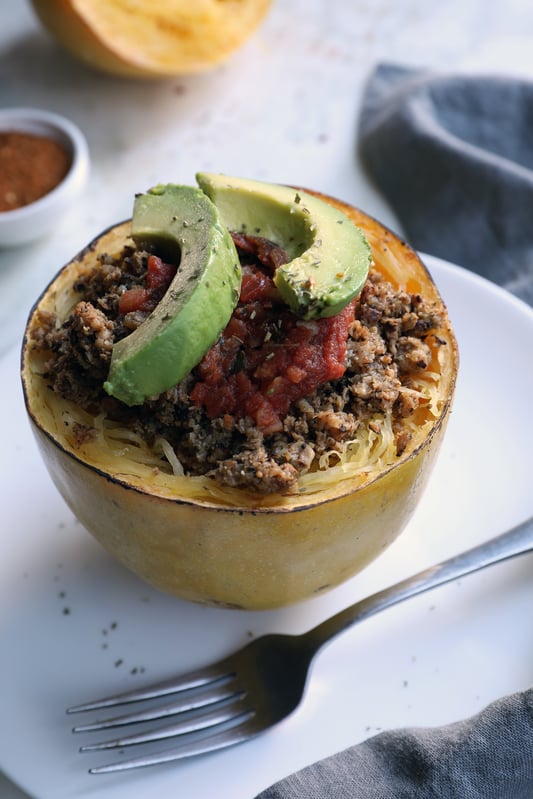 Half of spaghetti squash filled with mushrooms, herbs, avocado, salsa on plate with fork