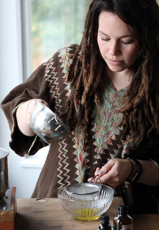 Woman pouring liquid out of double boiler and through sieve and into a bowl. 