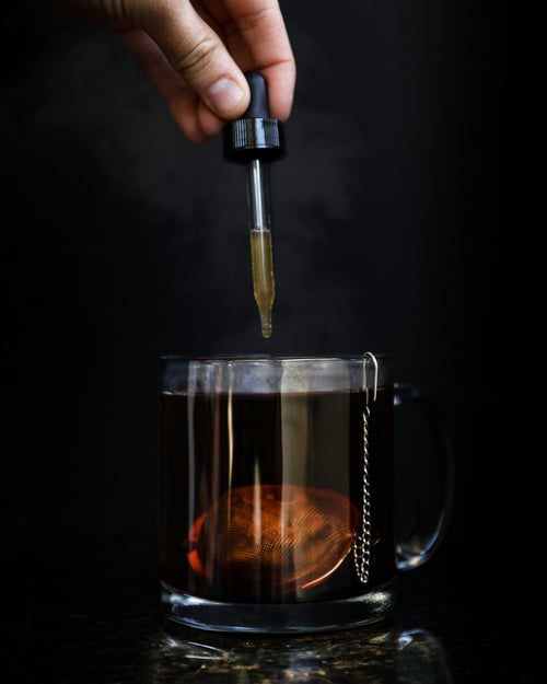 Hand using a medical dropper to add a tincture to tea