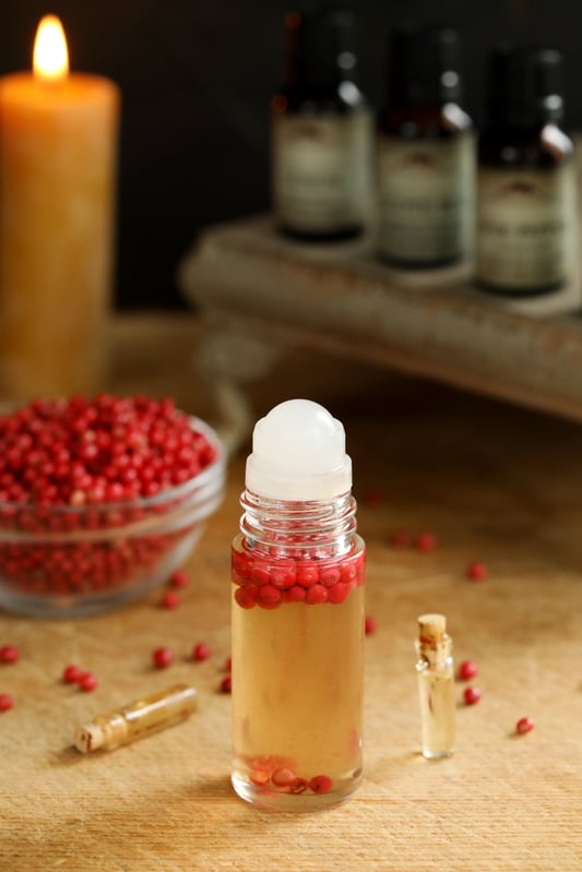 A sweet and spicy essential oil blend for fall uses pink peppercorns in a roll-top bottle.