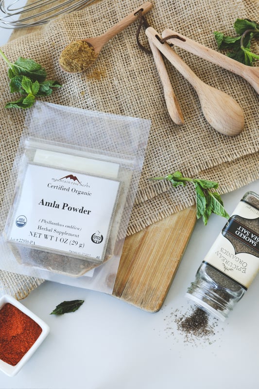 Bag of amla powder, smoked sea salt, mint leaves, and wooden spoons for making amla drink