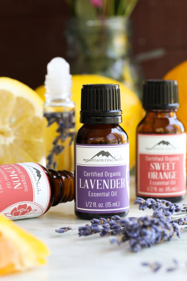 Bottles of lemon, sweet orange and lavender essential oils with fresh lavender and lemons slices.