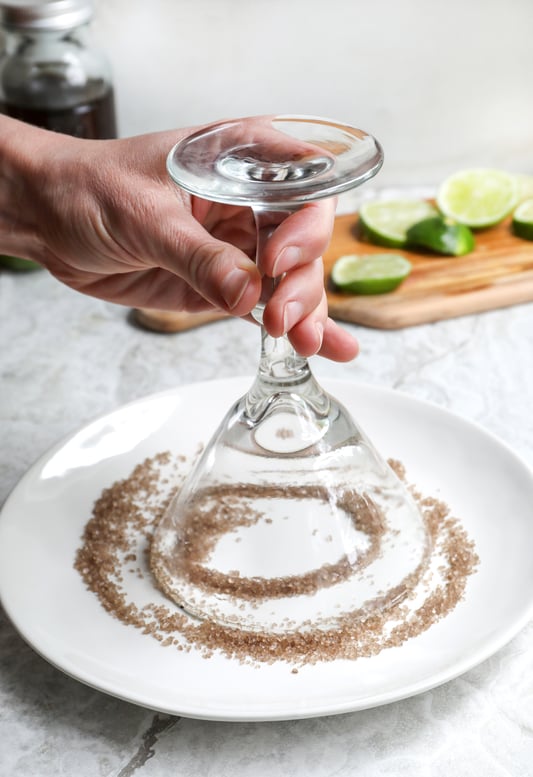 Hand holding margarita glass face down to cover rim with salt