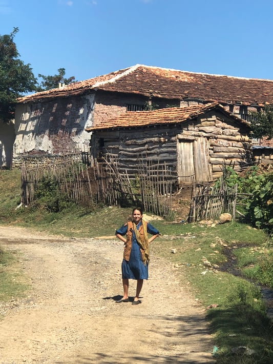 Susan Leopold of United Plant Savers poses in front of rustic log and brick farmstead in the Albanian countryside.