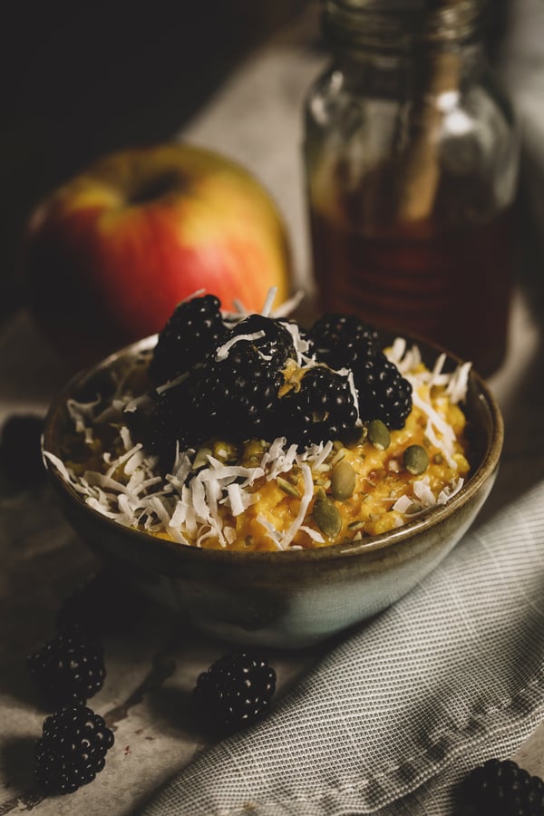 Bowl of golden congee with blackberries, coconut and pepitas.