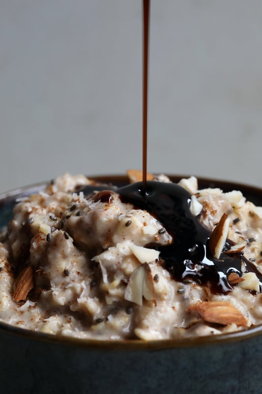 Elder berry syrup being drizzled on top of a bowl of oatmeal with almonds and chia seeds