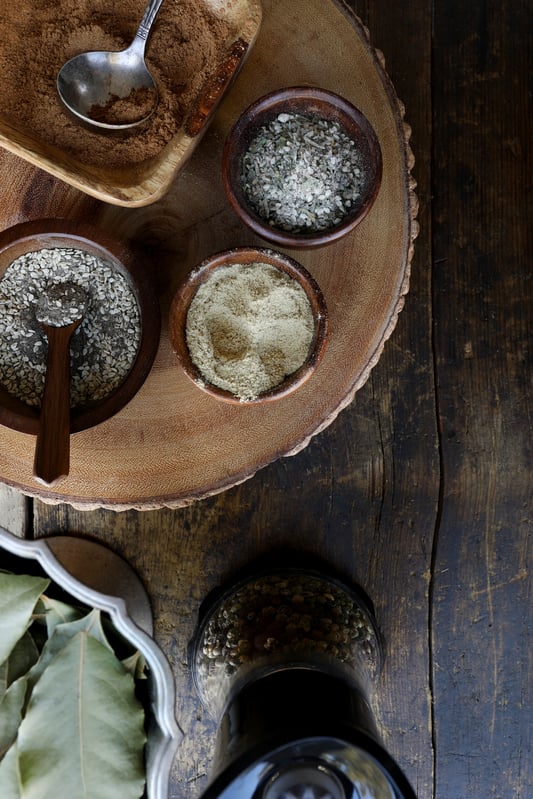 Wooden platter with small bowls of colorful herbs in a rustic setting. 