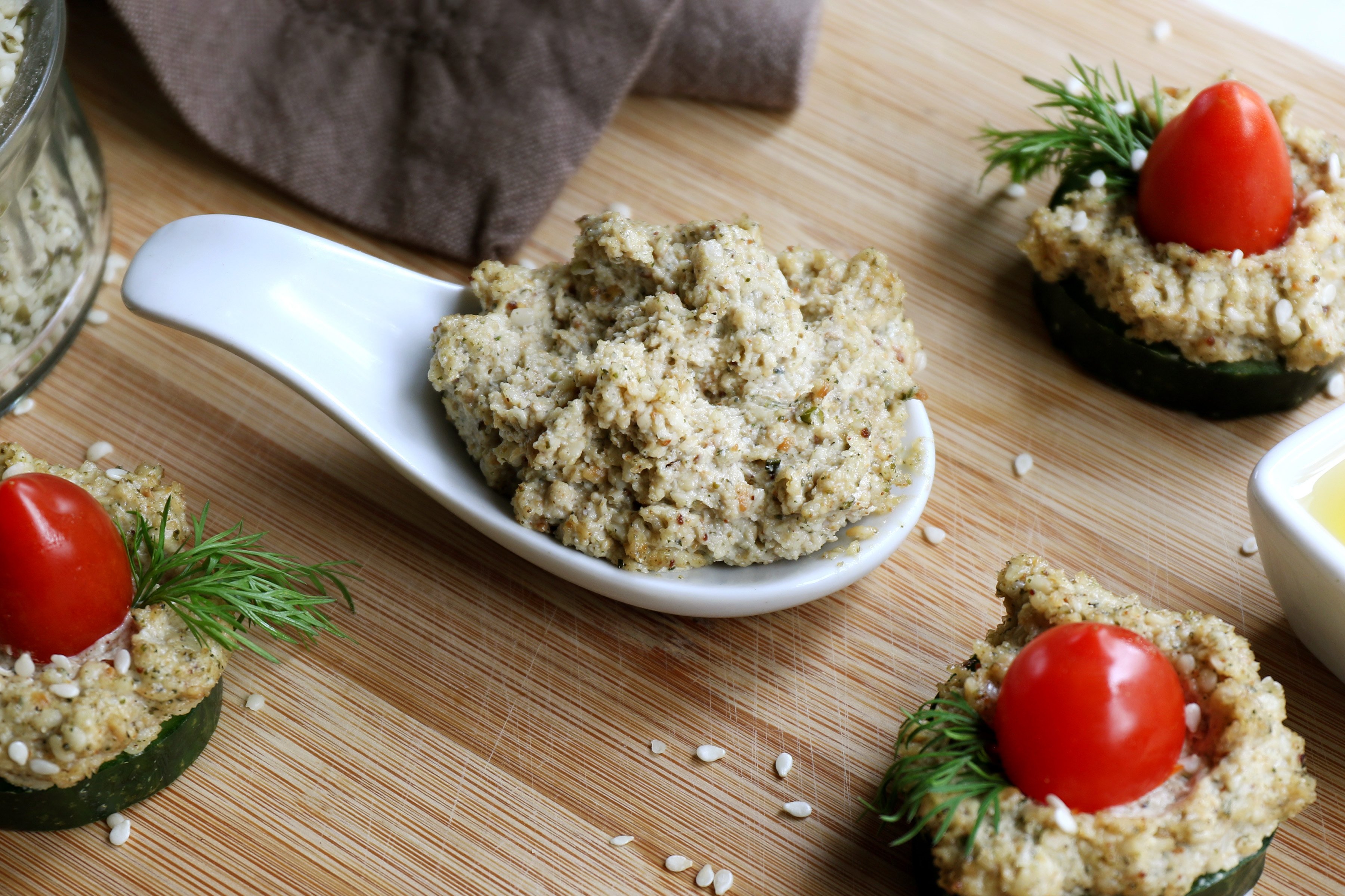 Organic homemade Tahini in a serving spoon with appetizers made with fresh cucumber, cherry tomatoes, and dill. Made with sesame seeds, hemp seeds, and pumpkin seed oil. 