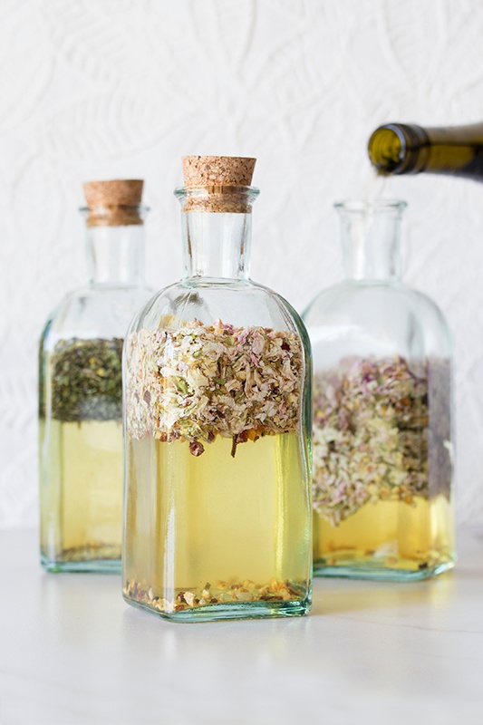 Three glass bottles with cork tops and herbs infused in wine 