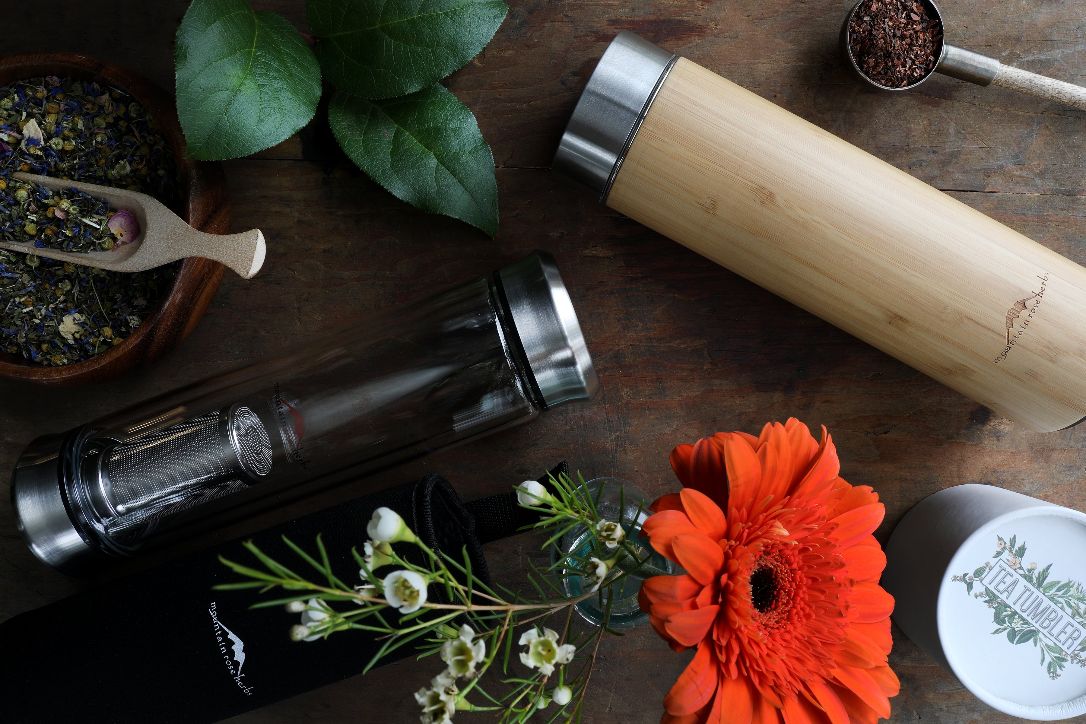 Wooden and glass hot beverage containers sirrounded by colorful flowers, plants and herbal teas. 