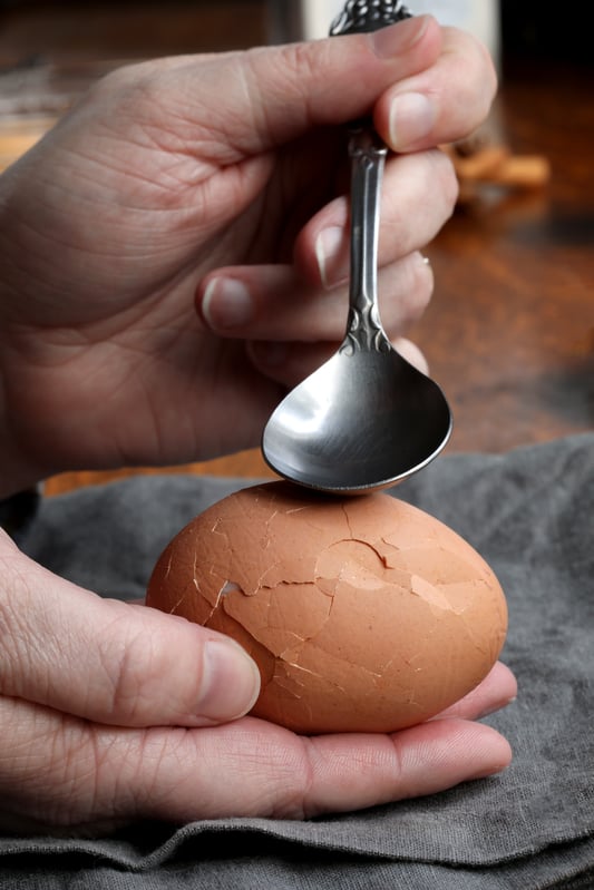 Hand holding spoon using utensil to crack marbled tea egg in palm of hand