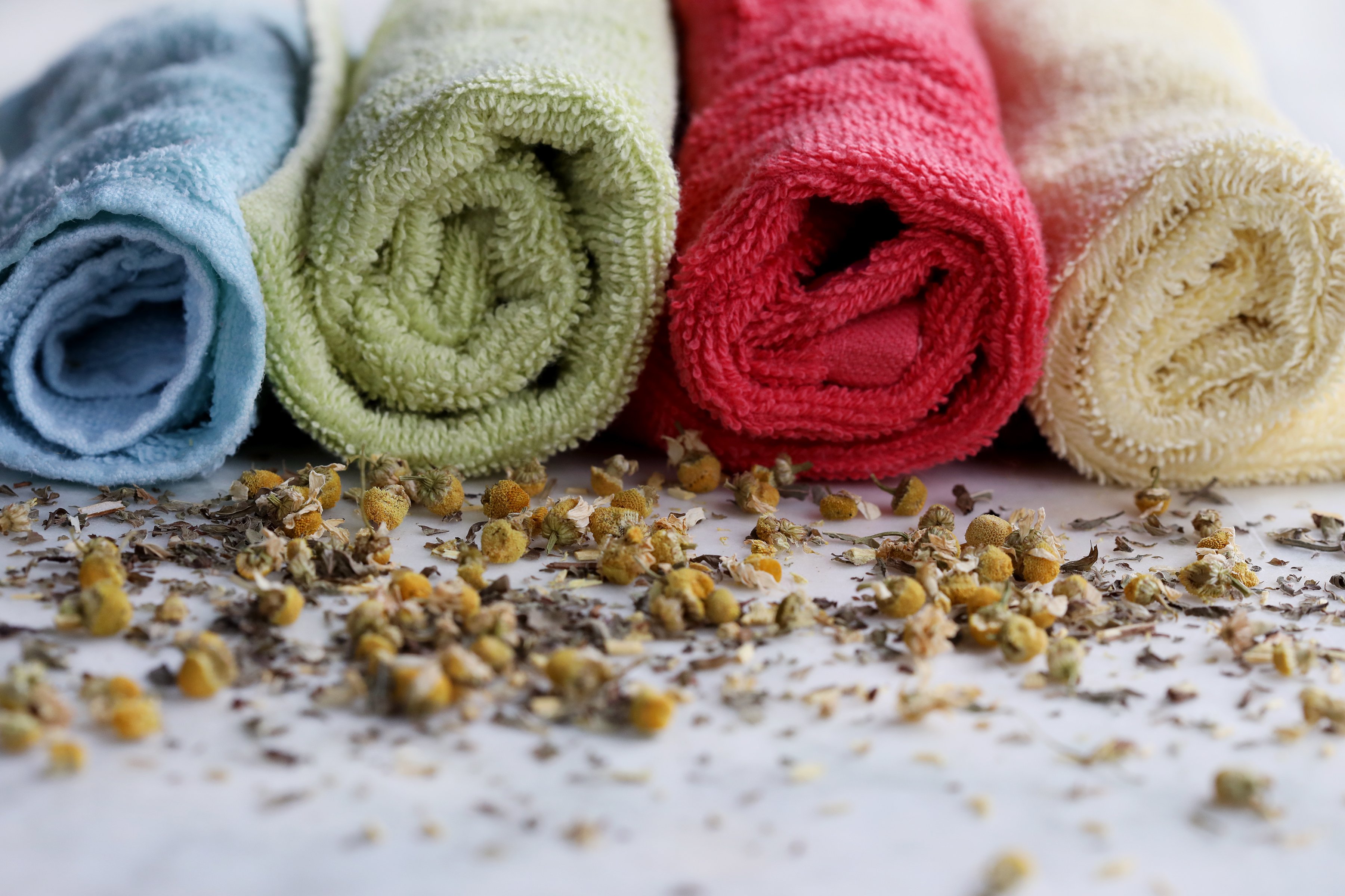 Colorful rolled towels with sprinkled chamomile on table in front of them. 