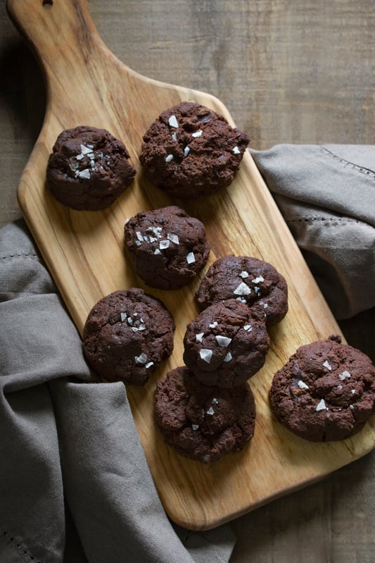 Chocolate cookies on a wooden paddle board sprinkled with flake salt. 