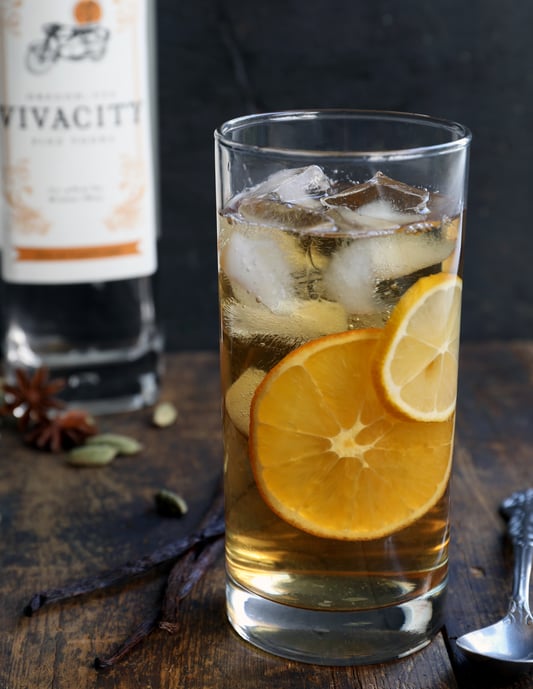 Tall glass with iced vermouth drink with lemon in it sitting on wooden table