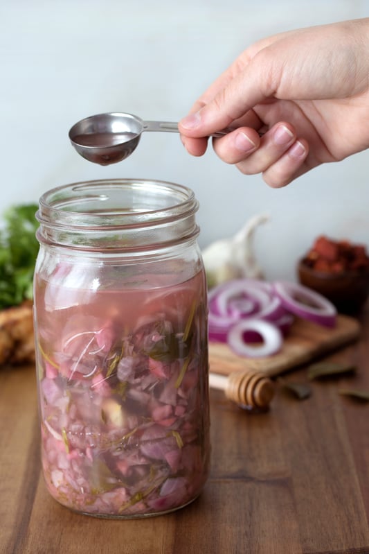 hand taking a tablespoon of fire cider from a mason jar