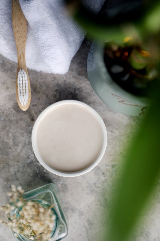 Wooden toothbrush next to bowl of homemade toothpaste with a crisp clean towel alongside. 