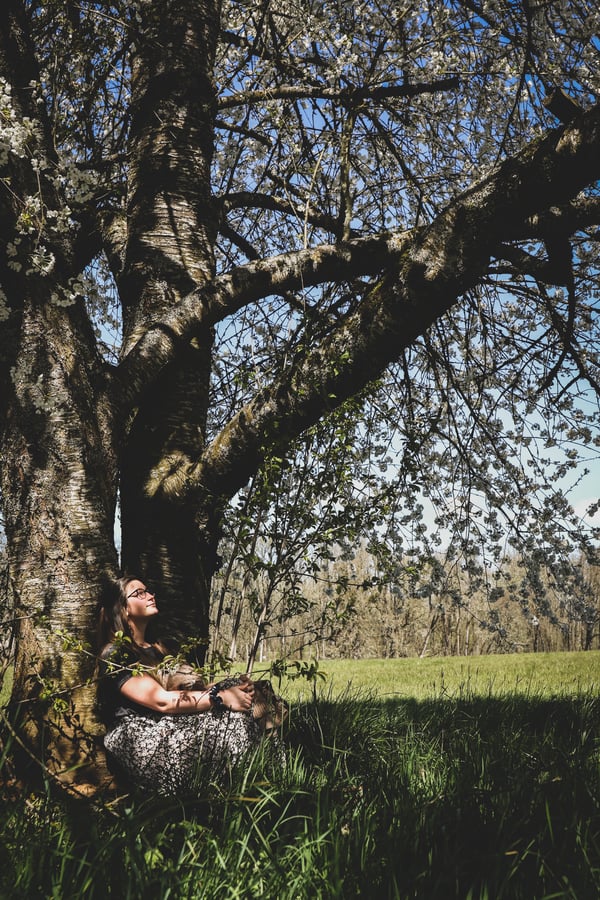 Woman sitting with her back to a tree in the forest.
