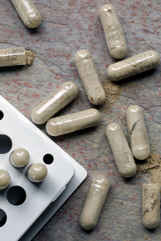 Capsules filled with triphala powder laying out on granite counter