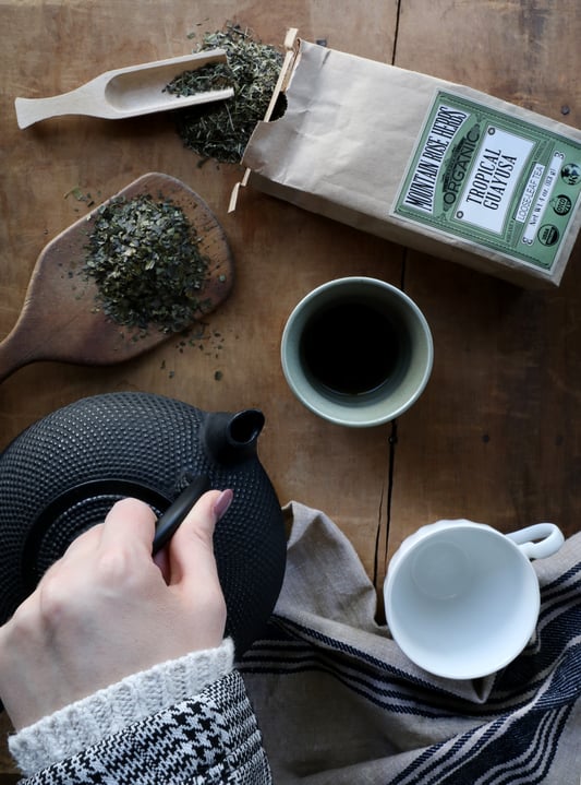 Display of tea being pouring out of cast iron tea pot with spilled tea on table and bag of Mountain Rose Herbs tea displayed.