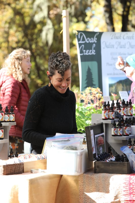 A vendor at a booth with many herbal products in an outdoor setting.