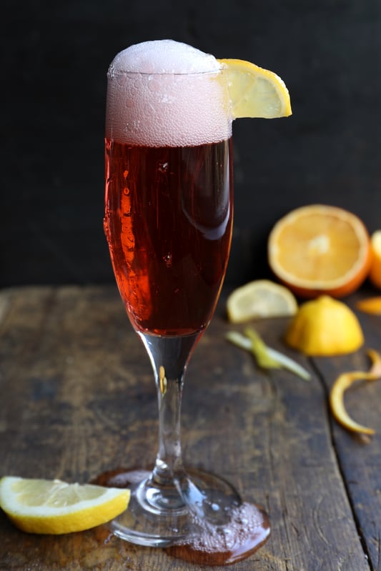 Red champagne drink with bubbly top, made with campari, vermouth, and organic gin