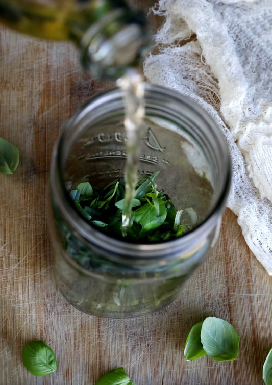 Pouring vingar into mason jar with fresh herbs.