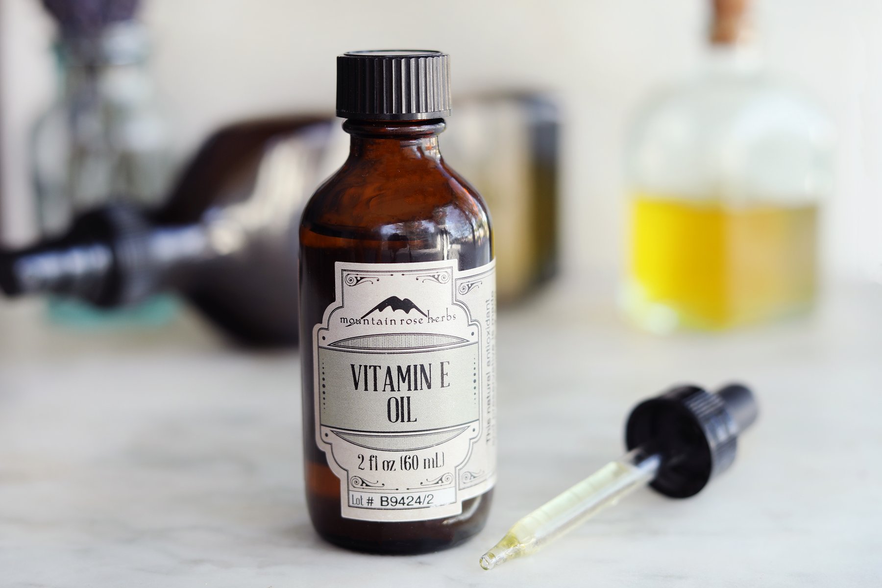 Bouteille d'huile de vitamine E avec un bouchon compte-gouttes et d'autres ingrédients de bricolage en arrière-plan.