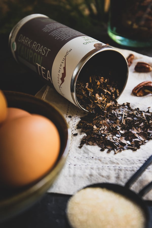 A tin of dark roast yaupon tea with tea spilling out