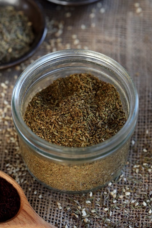 Za'atar spice blend in a clear glass jar with a rustic background.