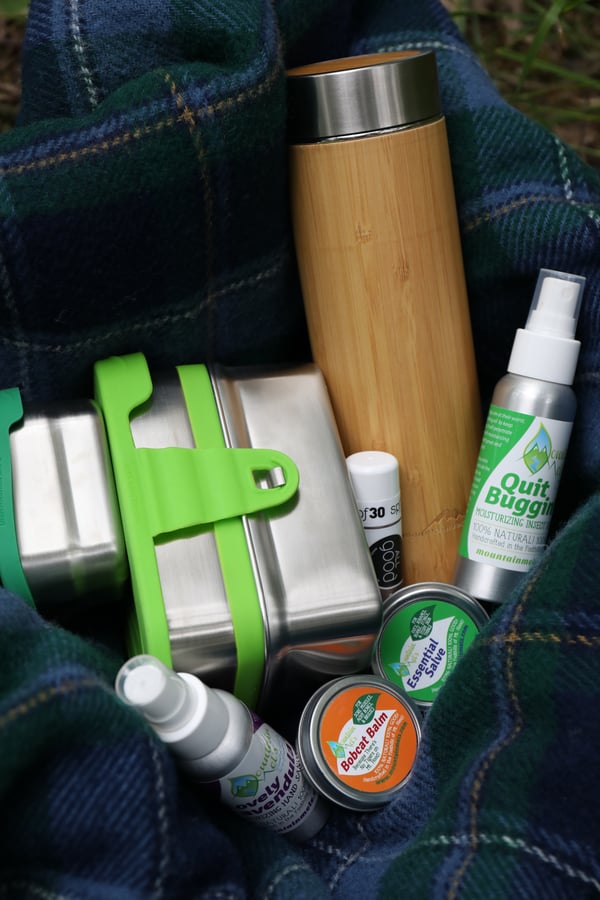 Various products are packed into a hiking backpack for an outdoor adventure. Bamboo tea tumbler, stainless steel food containers, and reusable tins and bottles for outdoor use.