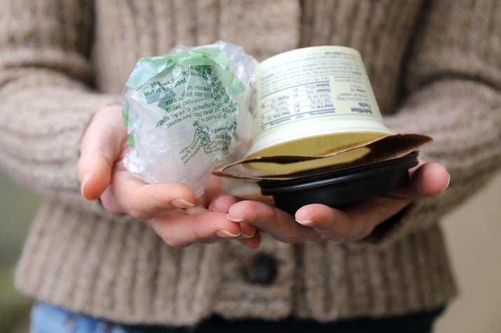 Hands holding plastic grocery bag and yogurt container and coffee holder in palm of hands
