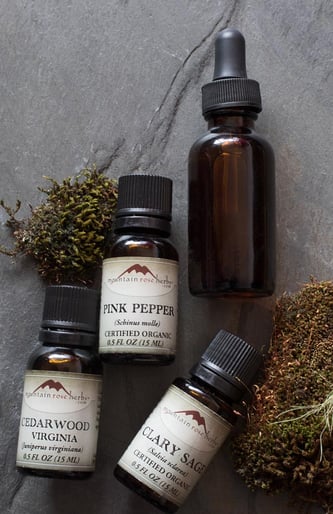 Pink Pepper Cedarwood Virginia and Clary Sage essential oils on a stone background with amber dropper bottle and moss