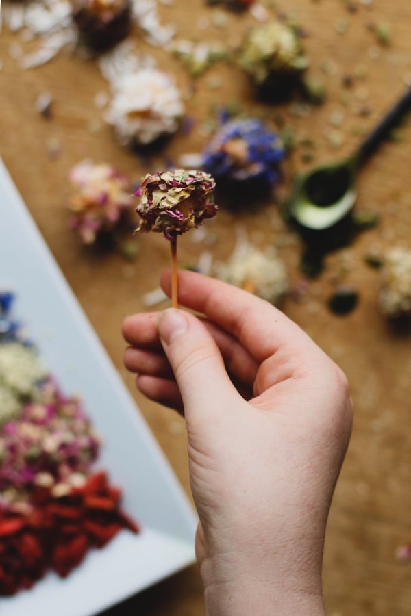 A vegan caramel apple bite dipped in rose petals on a toothpick