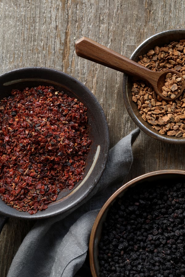 Bowls of herbs on a rustic table top are filled with dried rosehips, elderberries, and cinnamon chips.