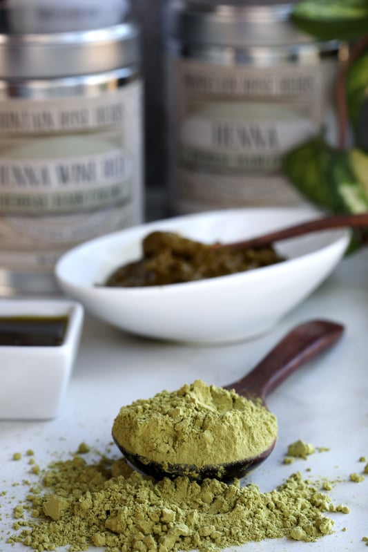 Spoon with green powder spilling out with henna tins and mixing bowl in background