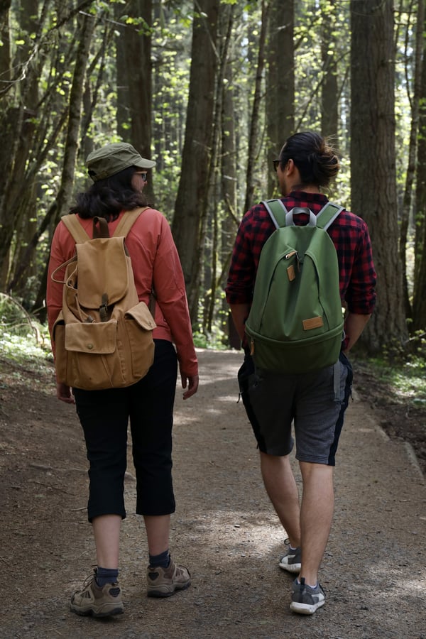 A young man and young woman hiking a forest trail with lightweight backpacks. 