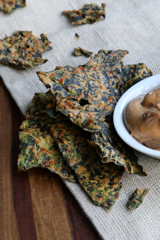 Detailed photograph of crispy kale chips and a bowl of spiced butter on a burlap table cloth.