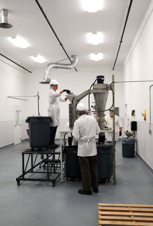 Three workers in lab coats and hard hats operating mill equiptment