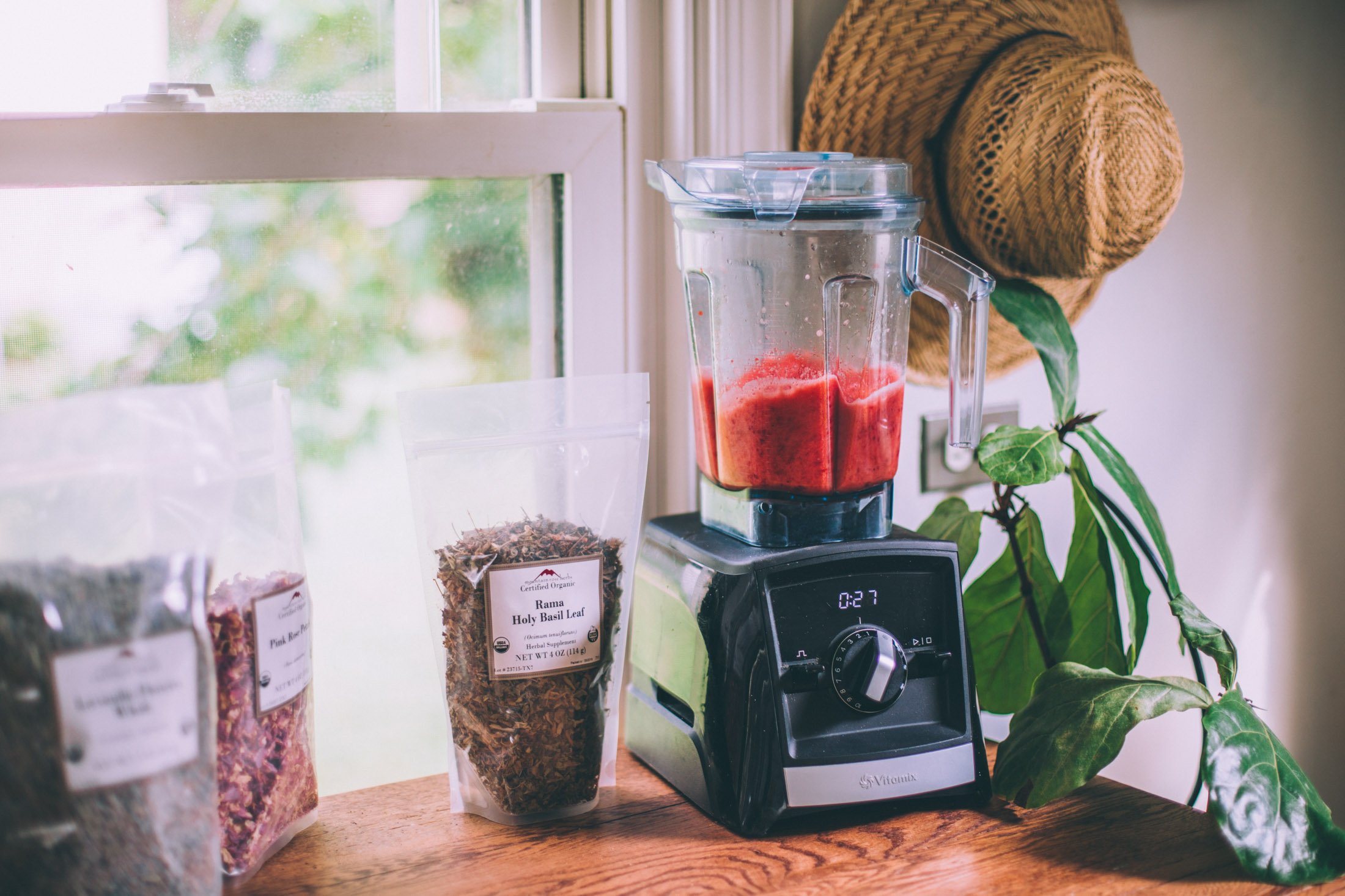 Preparations for making blended agua frescas. A Vitamix blender and bags of dried herbs like holy basil and rose petals.