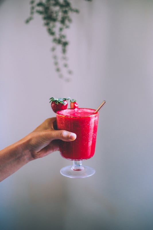 A blended strawberry agua fresca infused with herbal tea is prepared and ready for a hot summer day. A cocktail glass with a blended fruity beverage is garnished with fresh strawberries.
