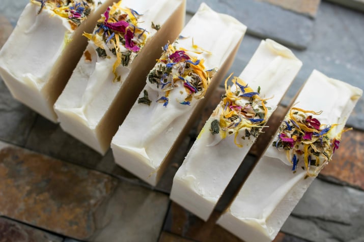 Fresh homemade bars of soap laying out with fresh herbs as a garnish