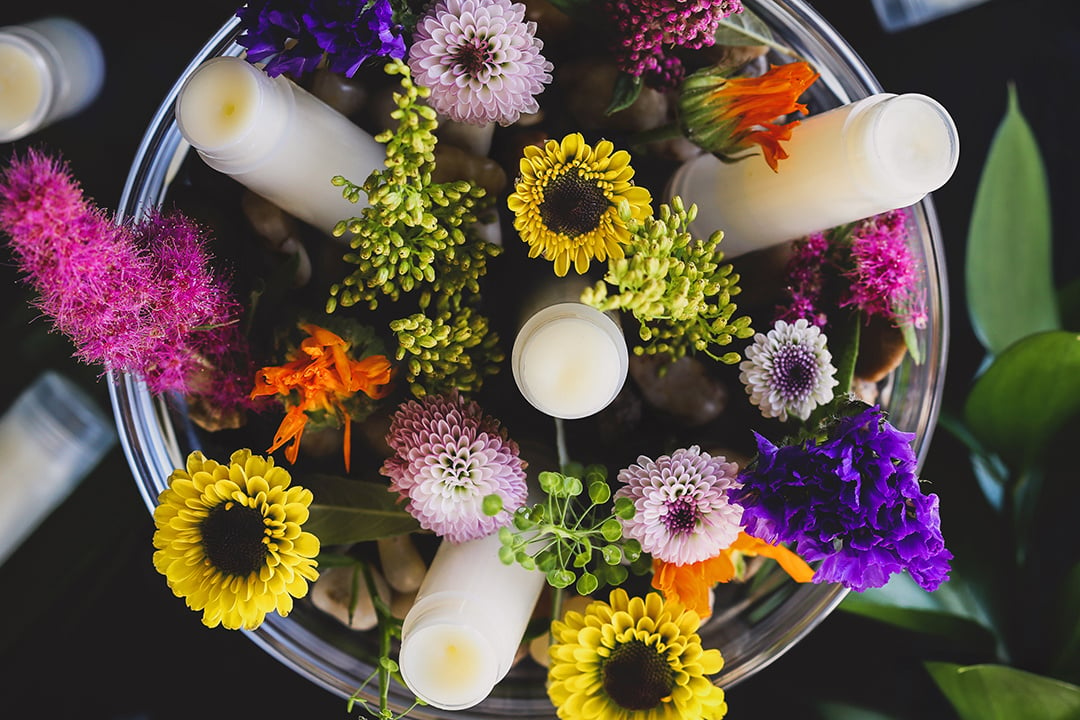 Homemade lip balm tube bowls surrounded by colorful fresh flowers. 