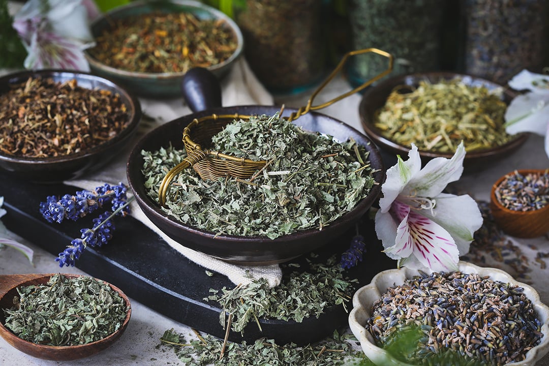 Bowls of colorful herbs surrounded by fresh flowers and a master copper tea infusion. 