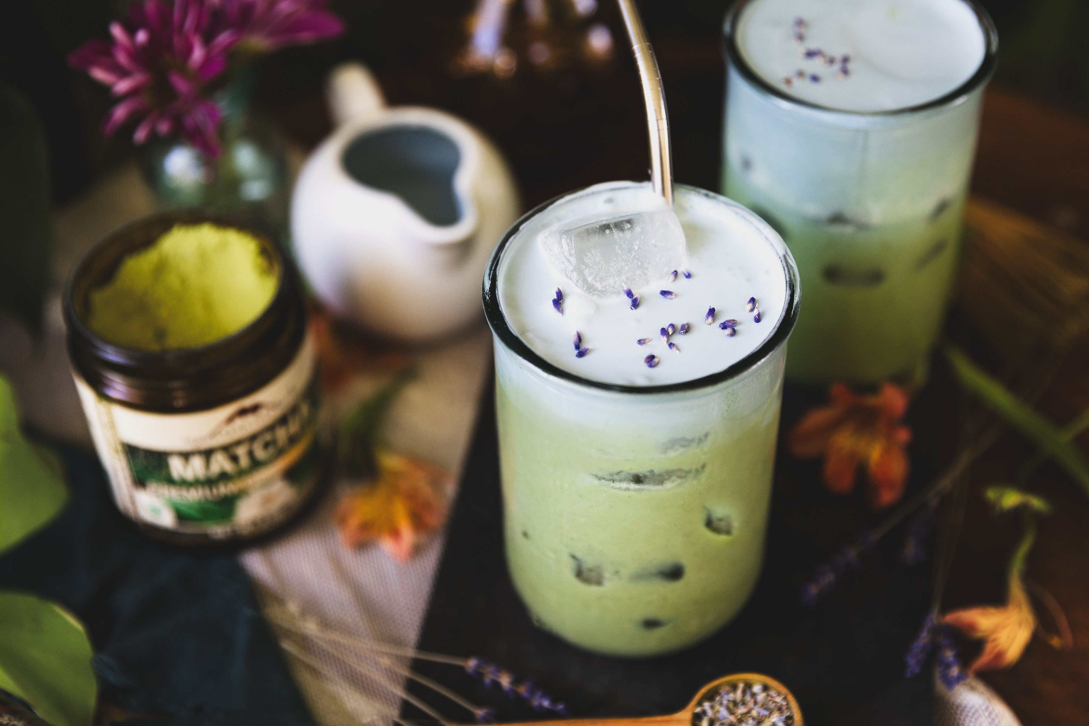 Clear glass filled with an iced green matcha latte with blue-hued lavender cold foam topping. 