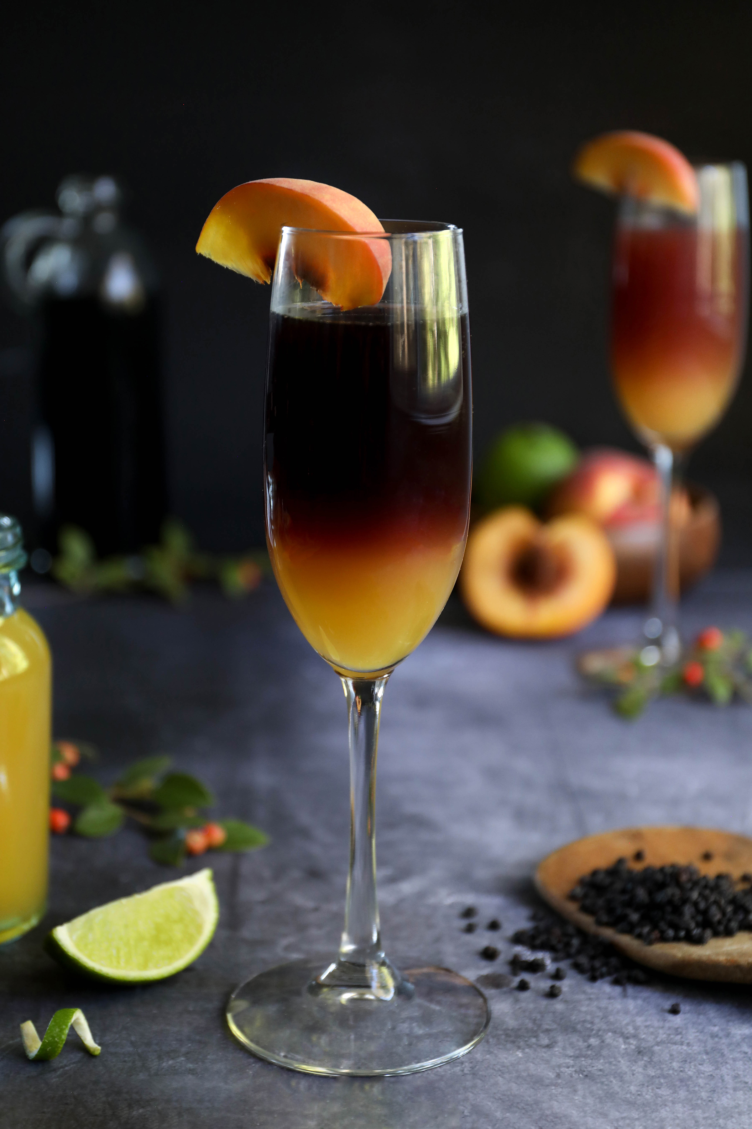 A two-tone elderberry peach Bellini in a champagne flute, topped by a slice of peach